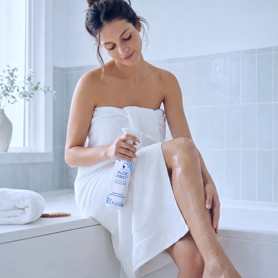 Femeie pulverizând Aloe First pe picior, pentru calmarea pielii după epilare sau ras